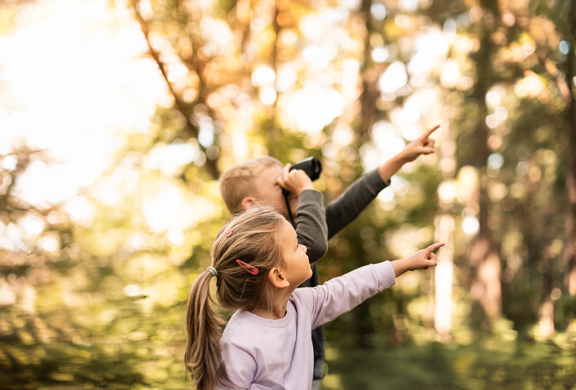 Children in the forest looking through binoculars exploring nature together.